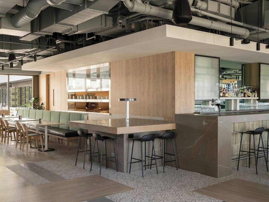 Un bar moderno con una barra alargada, taburetes y un área de estar con mesas y sillas.
