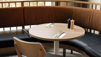 Een zithoek met een ronde tafel, een houten stoel en een zwarte lederen bank.