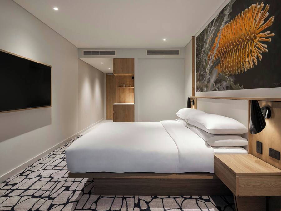 Habitación de hotel moderna con una cama grande, un televisor de pantalla plana, una mesita de noche de madera, un escritorio y un cuadro de una flor.