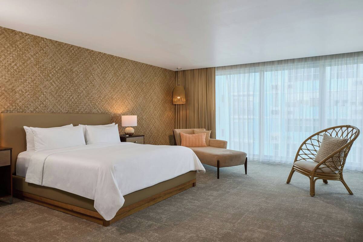 A hotel room with a large bed, a chair, a nightstand, and a lamp.