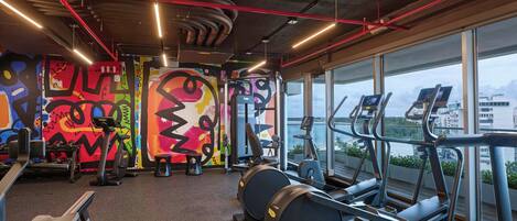 A gym with exercise equipment, a large window with a view, and colorful graffiti on the walls.