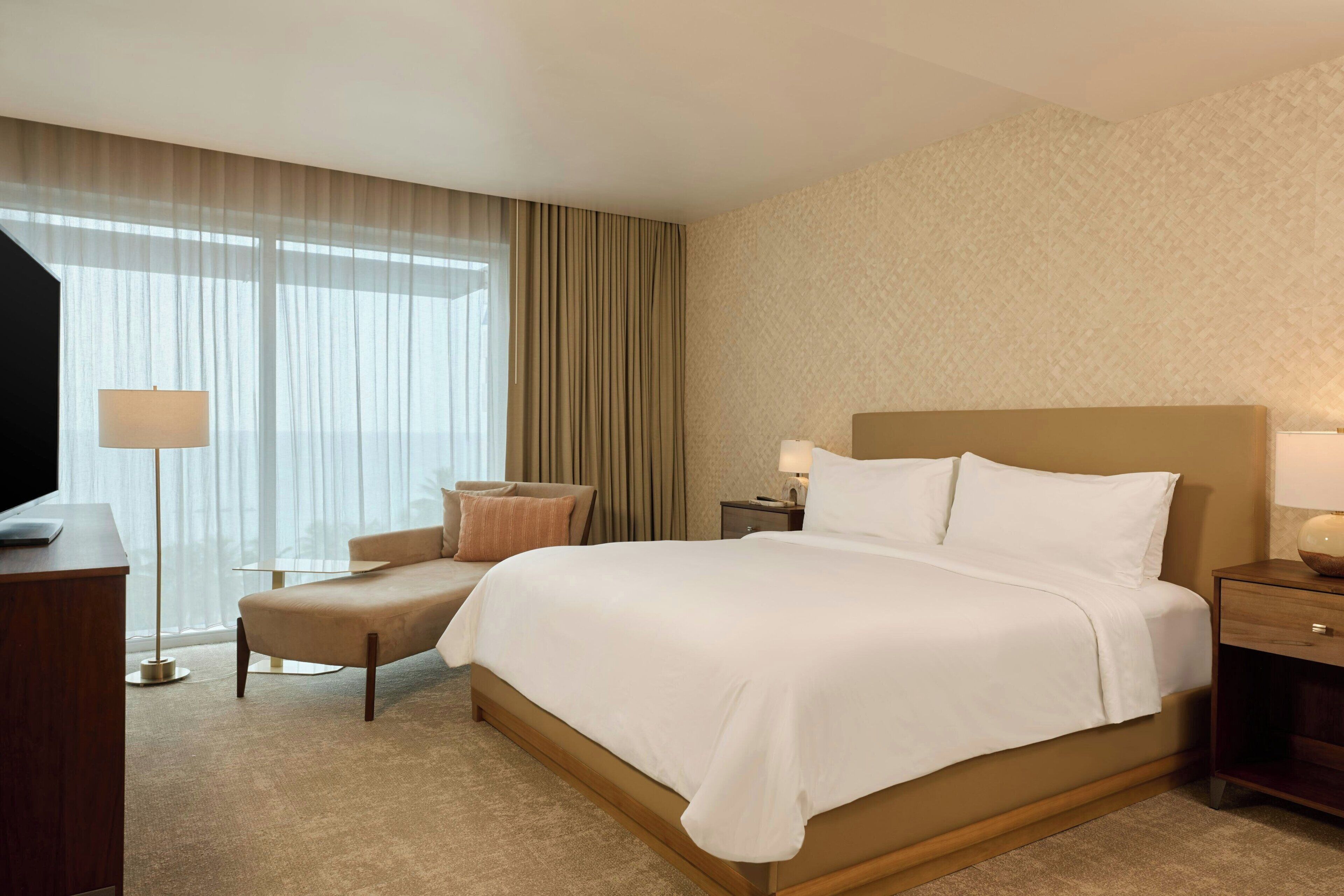 A hotel room with a large bed, a desk, a chair, and a TV.