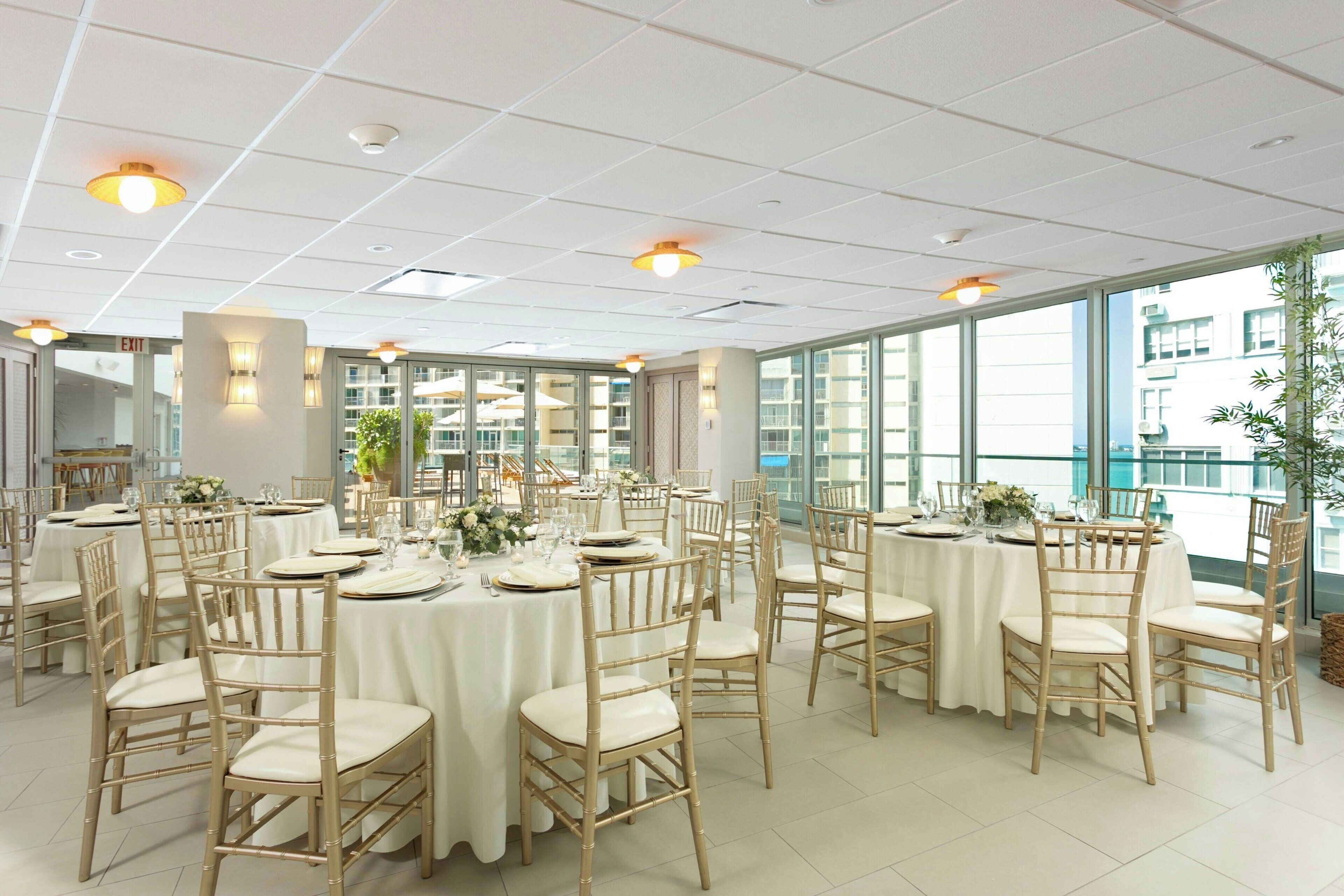 A spacious dining area with round tables, white tablecloths, and bamboo chairs.