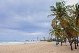 Una playa con palmeras, una orilla arenosa y un horizonte urbano.