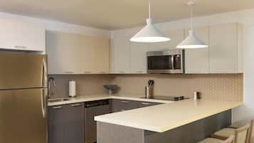 Una cocina moderna con un refrigerador de acero inoxidable, un microondas y un lavavajillas. Dos lámparas colgantes iluminan la isla.