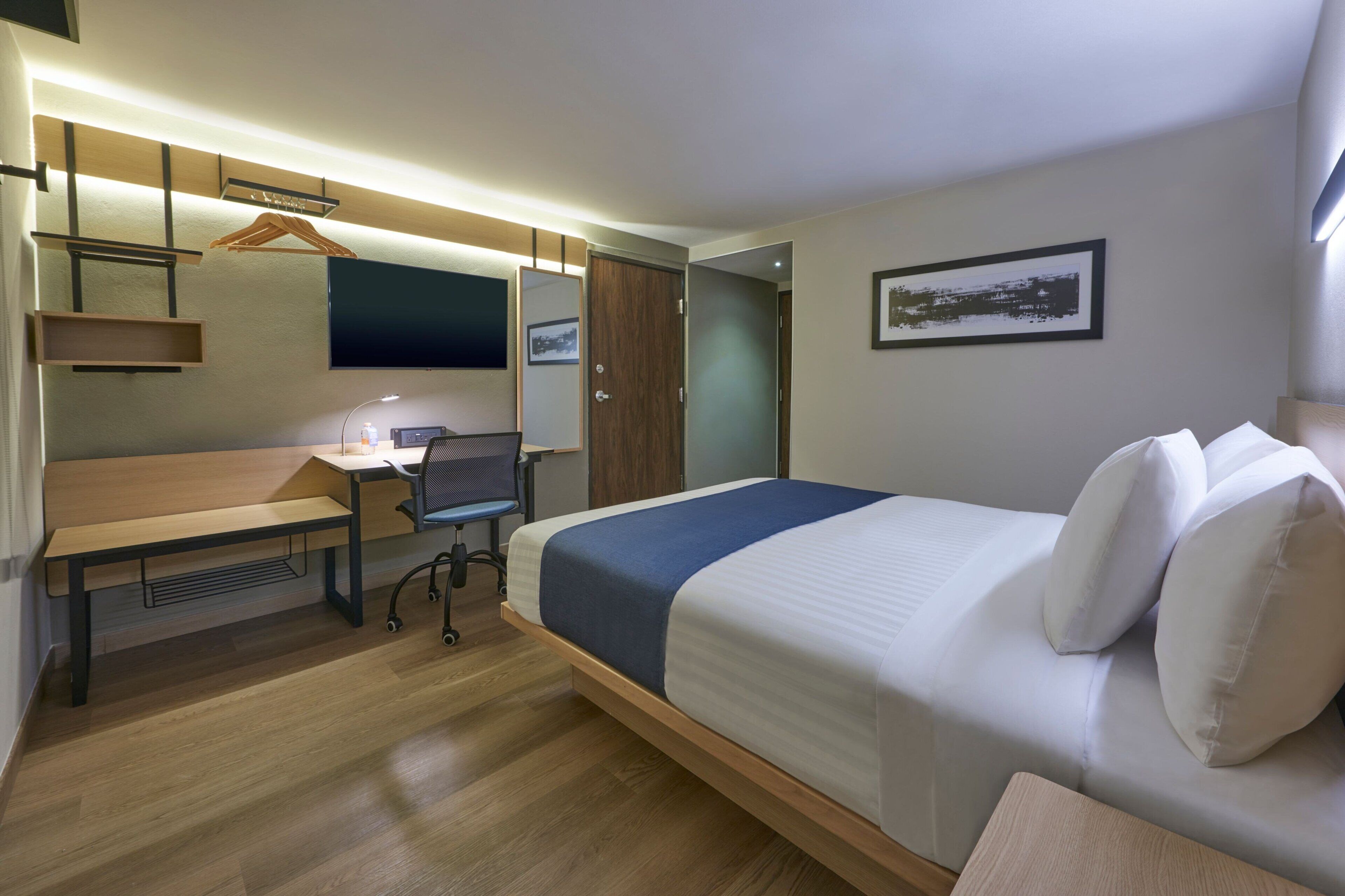 A modern hotel room with a bed, desk, chair, and a wardrobe.