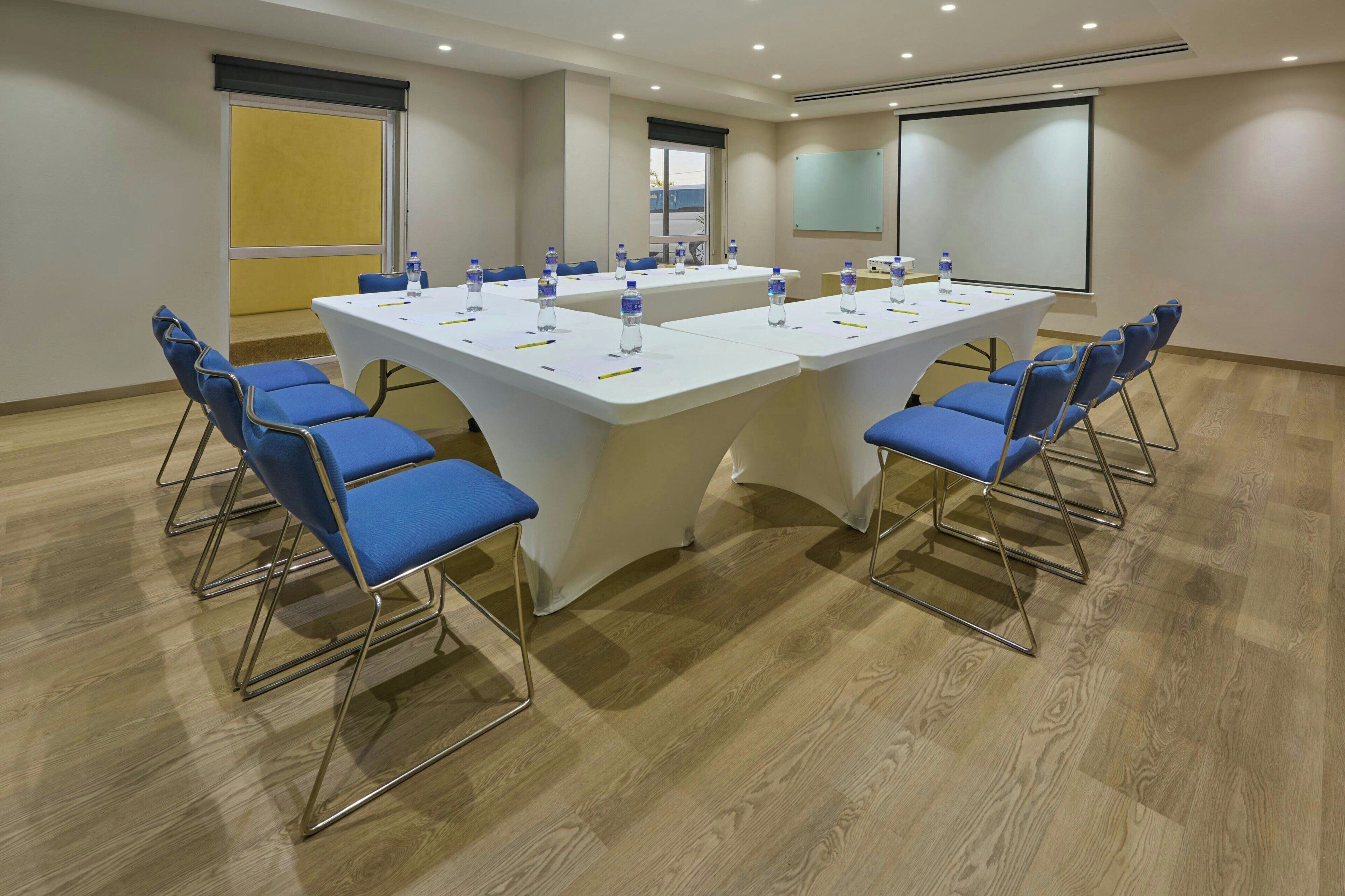A conference room with a large table, blue chairs, and a projector screen.