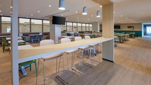 Una amplia cafetería con mesas largas, sillas y lámparas colgantes.