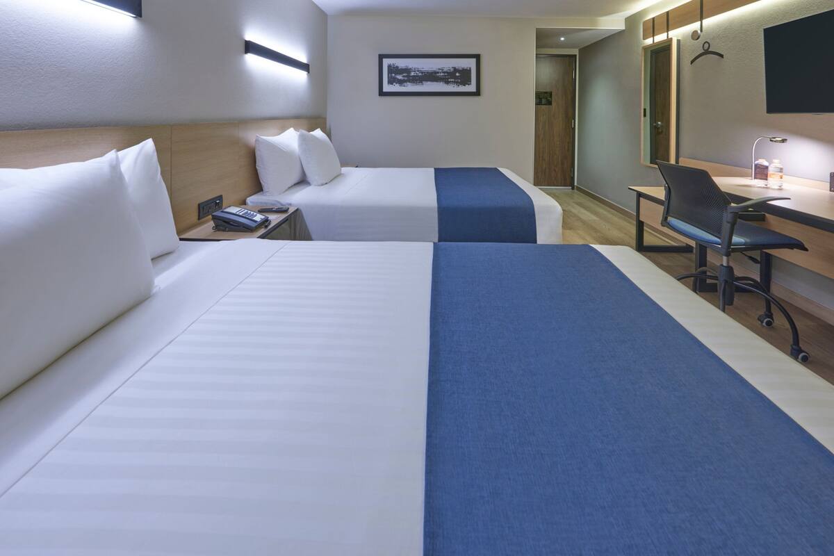 A hotel room with two beds, a desk, a chair, a telephone, and a framed picture on the wall.