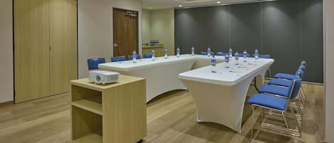 A conference room with a long table, blue chairs, a white tablecloth, and a projector on a stand.