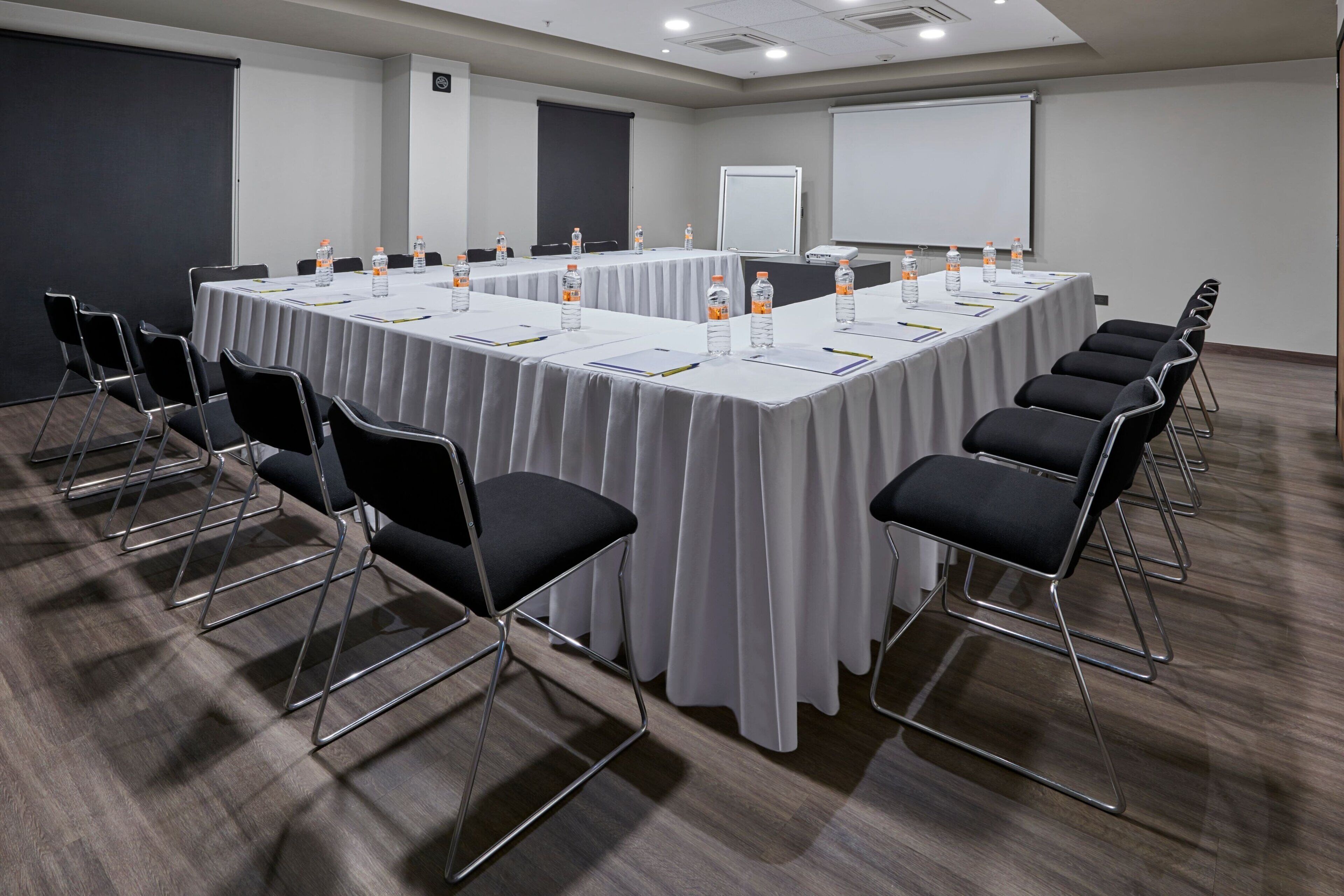 A conference room with a long table, chairs, water bottles, and a projector screen.