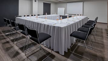 A conference room with a long table, chairs, water bottles, and a projector screen.