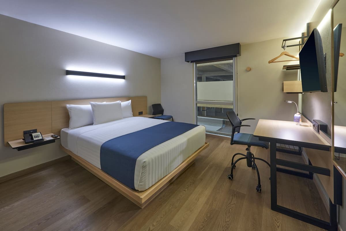 A modern hotel room with a wooden bed, a desk, and a chair.