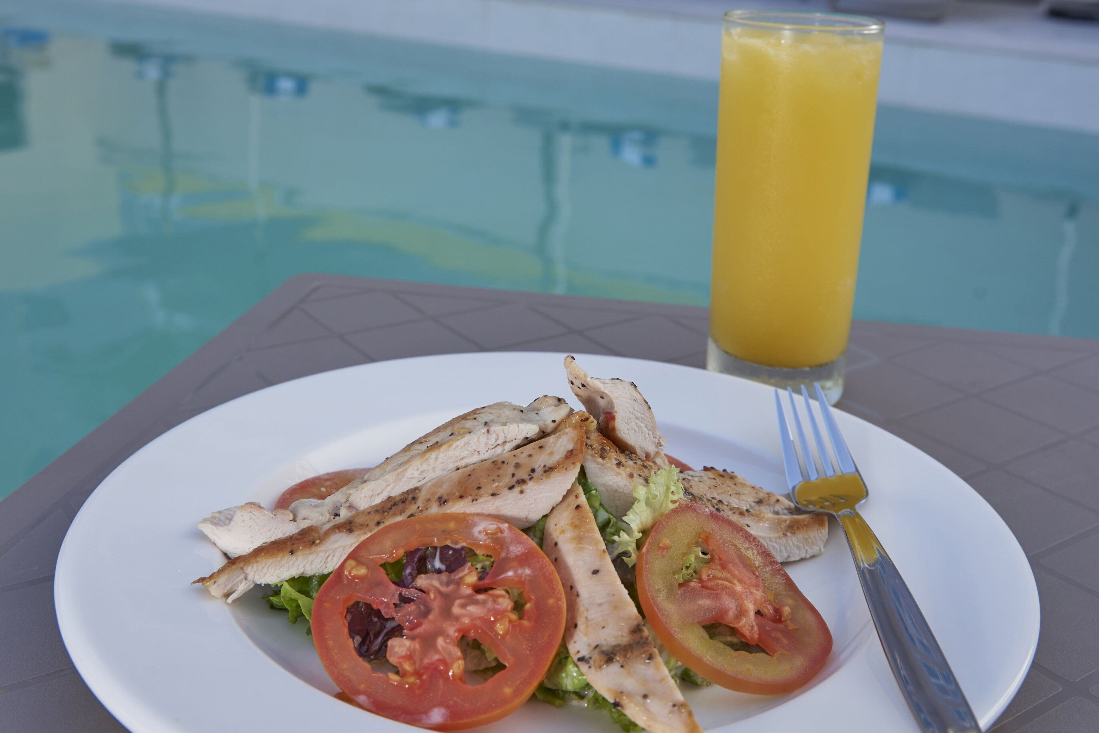 Un plato de pollo a la parrilla y verduras junto a una mesa al lado de la piscina.