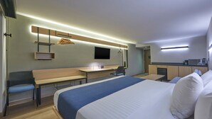Habitación de hotel moderna con una cama grande, un escritorio, una silla, un televisor y una kitchenette.
