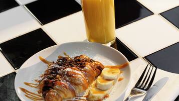 Um prato com sobremesa, um copo de suco de laranja e talheres sobre uma mesa xadrez.