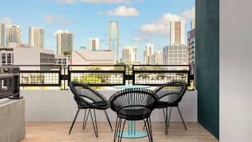 A balcony with a city view, featuring three black chairs and a small round table.