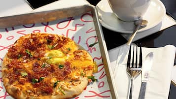 A breakfast setting with a pizza, a cup of coffee, and cutlery on a table.