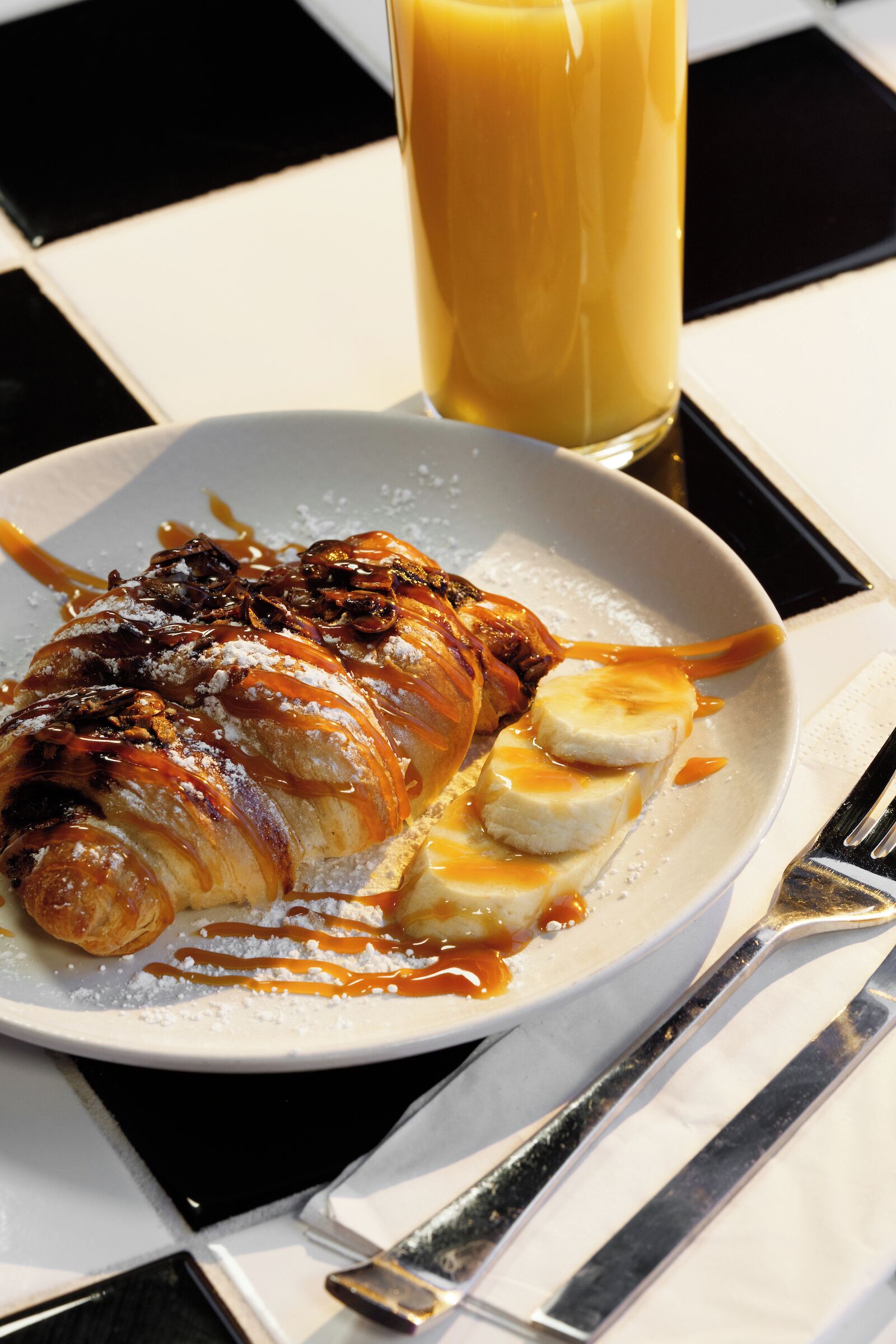 En tallerken med dessert, et glas appelsinjuice og en gaffel på et bord.