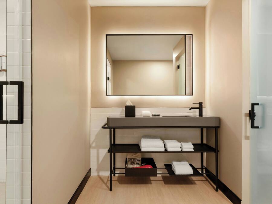 A modern bathroom with a large mirror, a sink, and a shelf with towels.