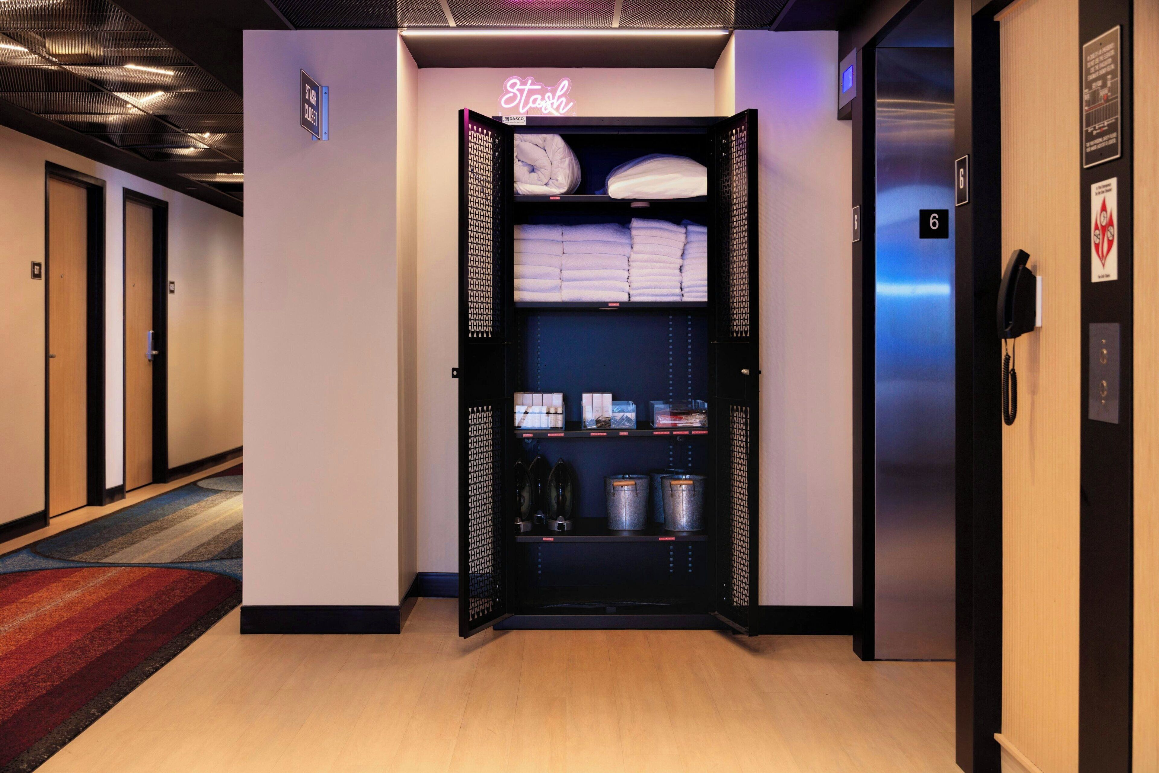 A hotel room with a closet containing folded towels, neatly arranged shoes, and storage bins.