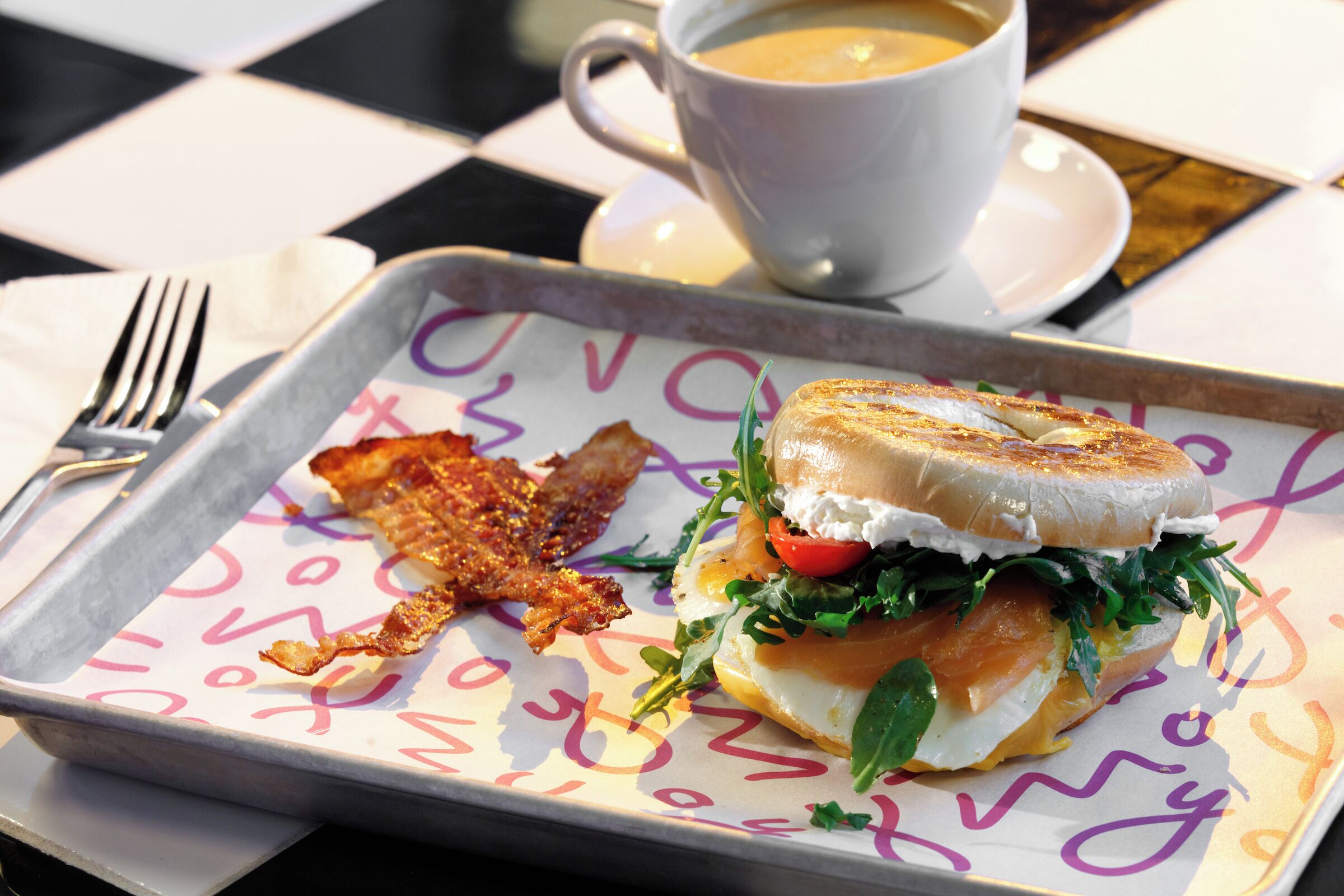 A sandwich on a tray with a cup of coffee in the background.