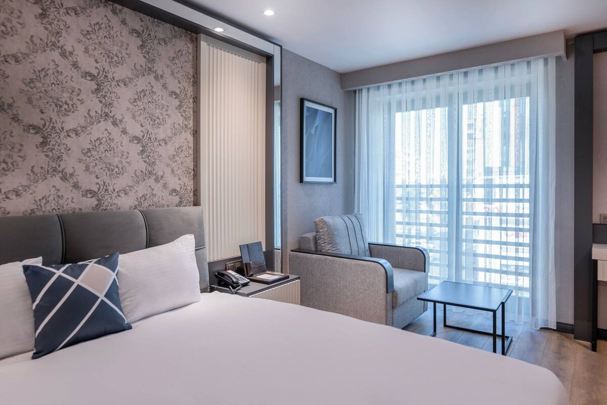 Une chambre d’hôtel moderne dotée d’un grand lit, d’un bureau, d’une chaise et offrant une vue sur la ville grâce à de grandes fenêtres.