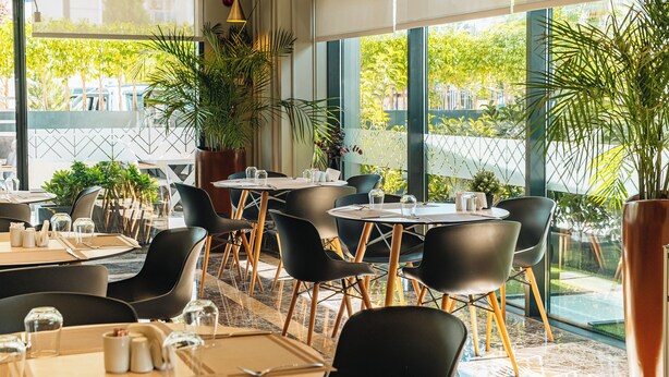 A restaurant with round tables, black chairs, and potted plants.