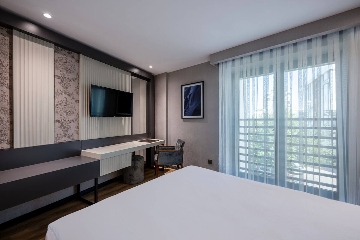 Une chambre d’hôtel moderne dotée d’un grand lit, d’un bureau avec une chaise, d’une télévision à écran plat et d’une fenêtre avec des rideaux.