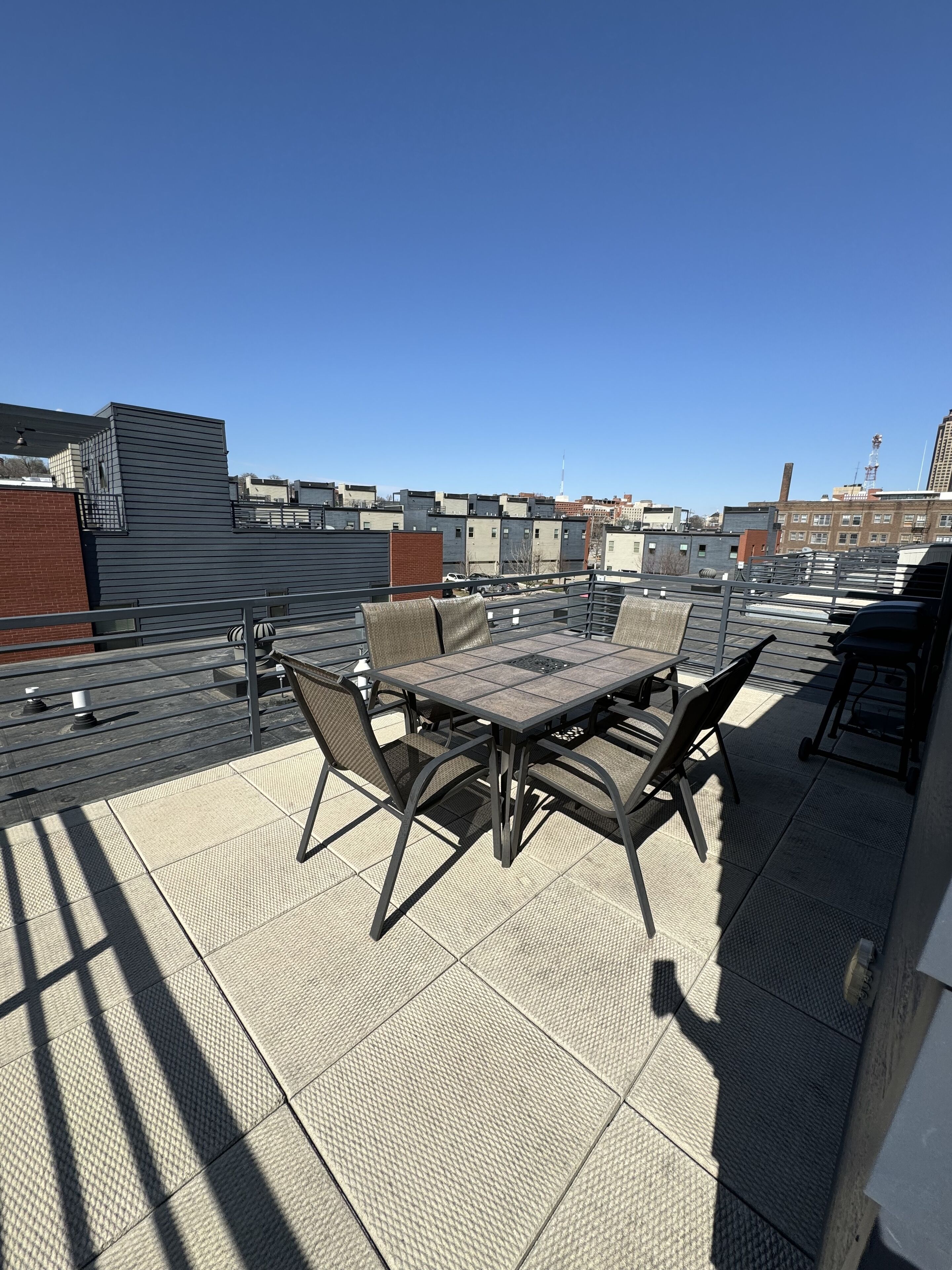 En takterrass med ett bord och stolar, ett räcke och utsikt över stadens silhuett.