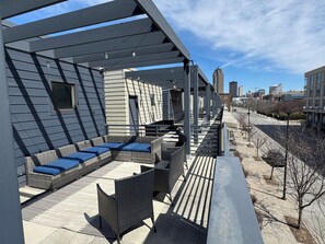 Une terrasse sur le toit, aménagée avec du mobilier d’extérieur, une pergola et offrant une vue sur la ville.