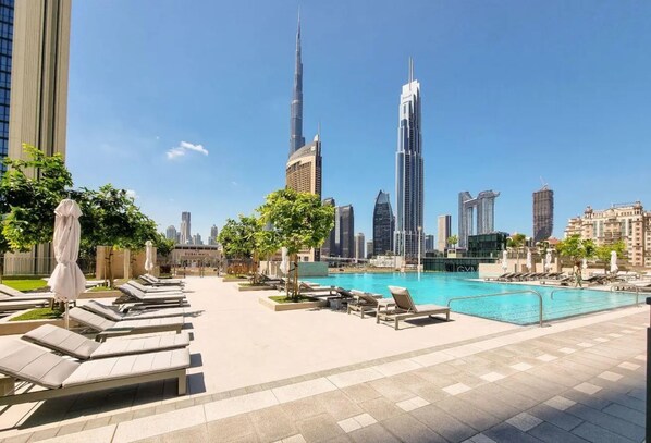 A rooftop pool area with lounge chairs and a view of the Dubai skyline, including the Burj Khalifa.