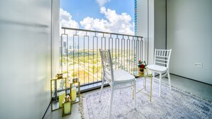 A balcony with a white chair, a small table with a vase, and a view of a cityscape. - Stylish 1BR with DIFC Skyline and Zabeel Views (Downtown)