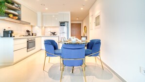 A modern kitchen with white cabinets, a built-in microwave, and a dining area with blue chairs and a round table. - Stylish 1BR with DIFC Skyline and Zabeel Views (Downtown)