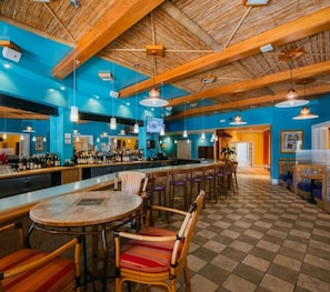A bar area with a checkered floor, wooden ceiling beams, and a bar counter with bottles and glasses.
