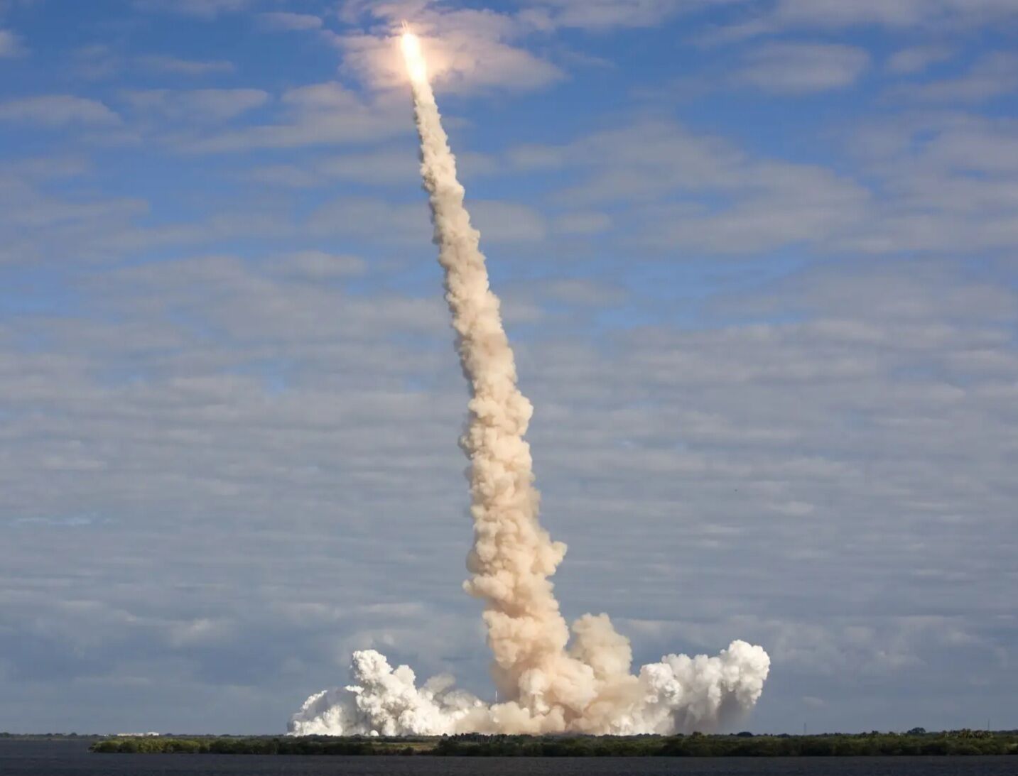 Raketenstart mit einer Rauchspur vor blauem Himmel.
