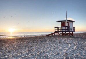 A lifeguard tower on a beach with the sun setting in the background.