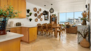 A spacious kitchen with wooden cabinets, a dining area with wicker chairs, and a view of the sea. - Stunning Bantry Bay Haven - Beach on Your Doorstep (Cape Town)