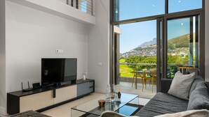A modern living room with a large TV, glass coffee table, and a sofa. - Lux Elegance in Heart of Mouille Point (Cape Town)