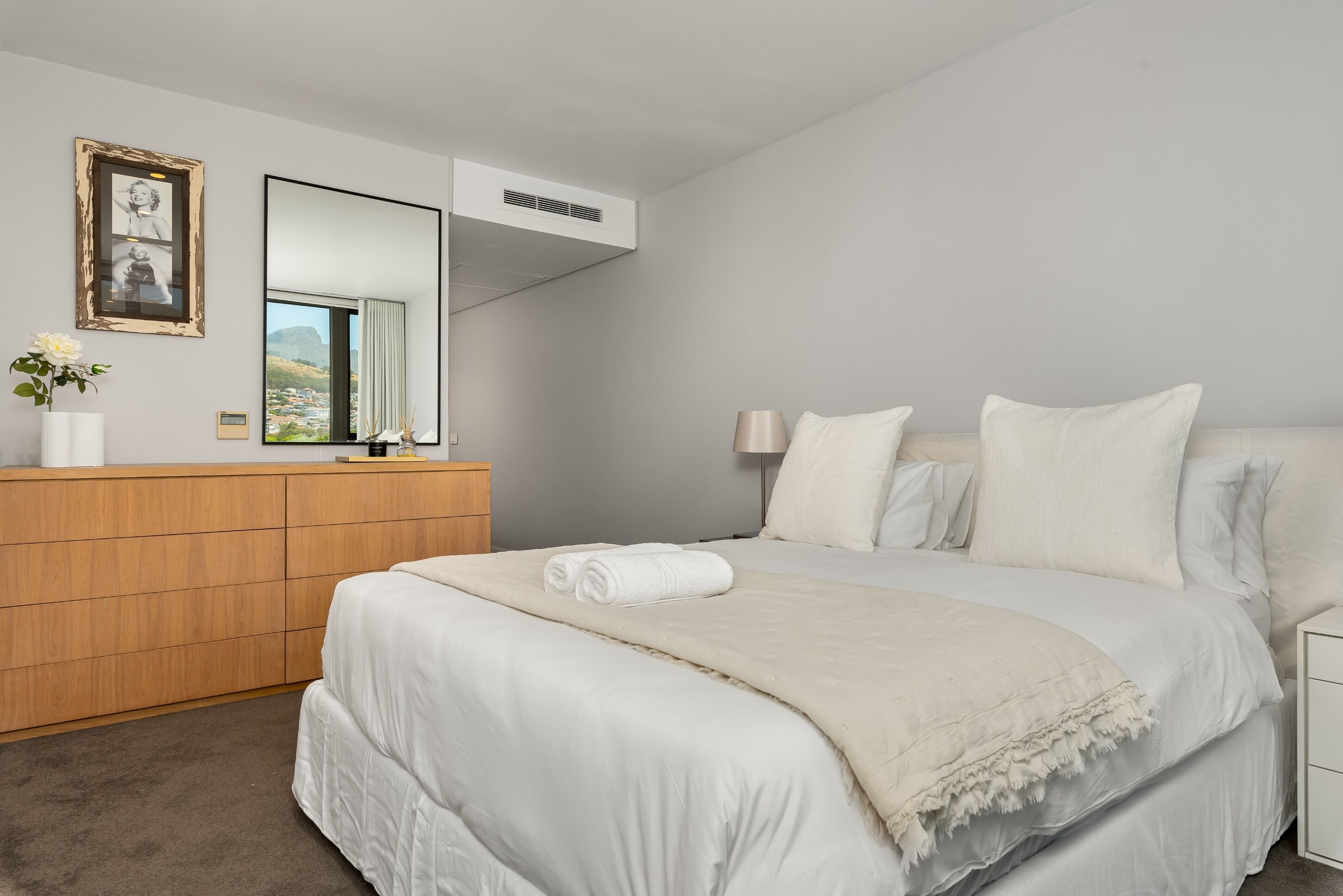 A bedroom with a large bed, a wooden dresser, a mirror, and a framed picture on the wall.