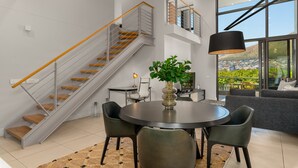 A modern interior with a staircase, dining area, and large windows offering a city view. - Lux Elegance in Heart of Mouille Point (Cape Town)