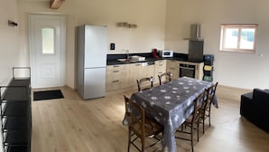 A compact kitchen with a refrigerator, microwave, and stove. There is a dining table with chairs and a black sofa.