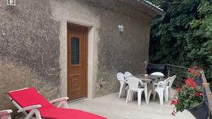 A patio with two sun loungers, a table with chairs, and a grill.