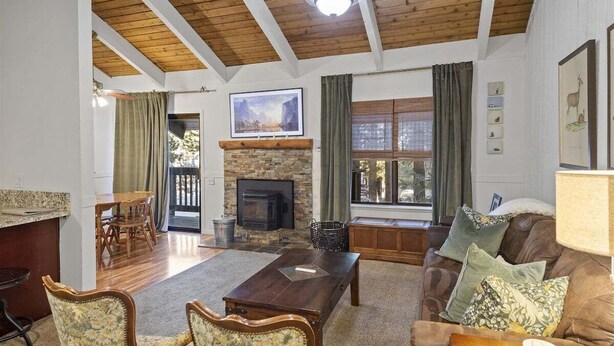 A cozy living room with a fireplace, wooden ceiling beams, a dining area, and a sofa with cushions. - Sunshine Village 126: Pet friendly, Close to Green (Mammoth Lakes)