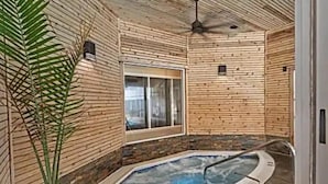 Un cuarto de spa con un jacuzzi, paredes de madera, un ventanal y un ventilador de techo.