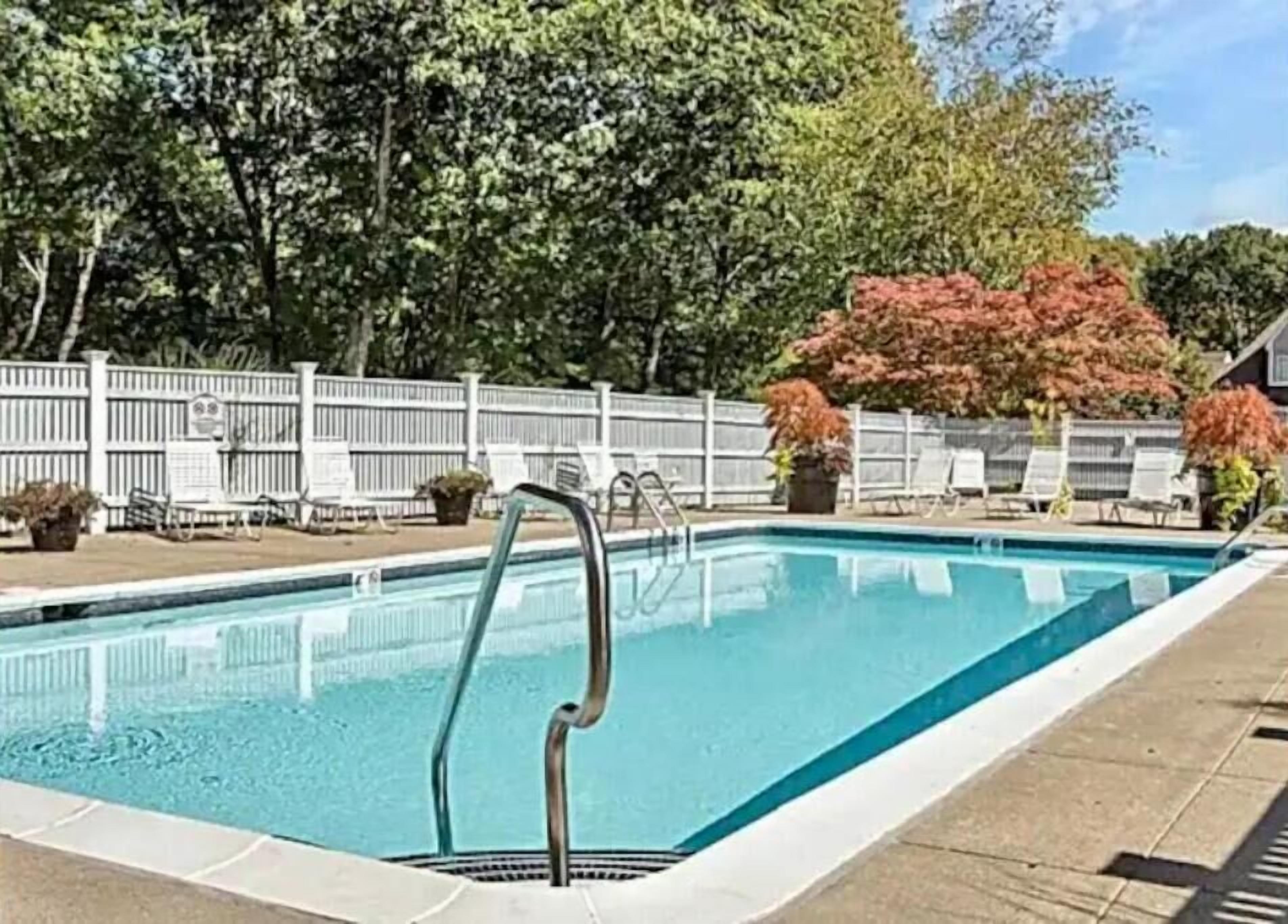 Une piscine rectangulaire avec un escalier en métal, entourée d’une clôture blanche et d’arbres.