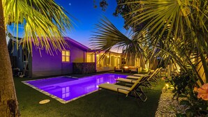 A backyard with a swimming pool, artificial grass, and lounge chairs.