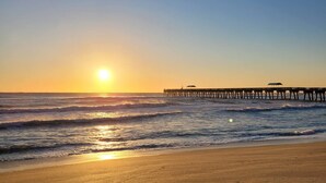 A beach with a pier extending into the ocean during sunset.