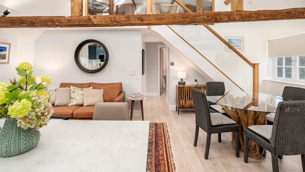 Ein geräumiges Loft mit hoher Decke, freiliegenden Holzbalken, einem Glastisch und einer gemütlichen Sitzecke mit Sofa und Sesseln.