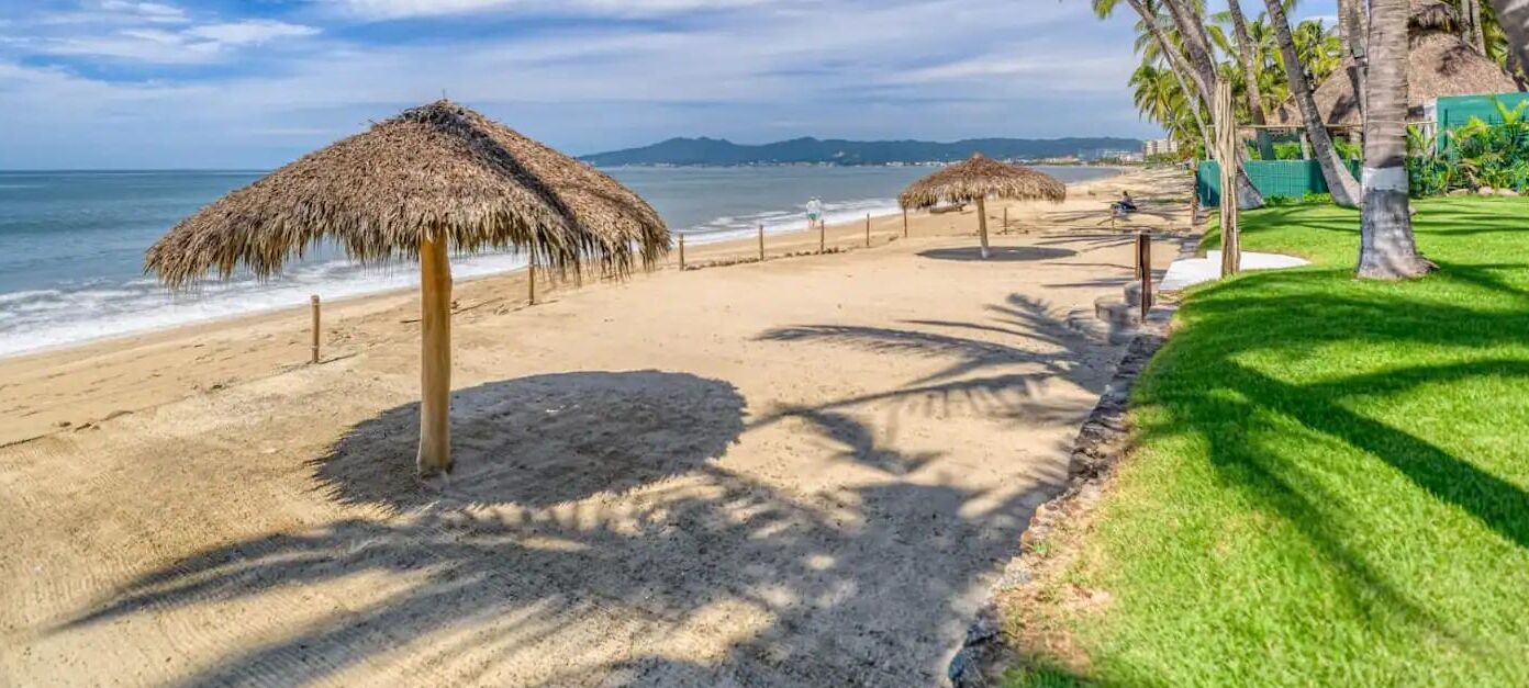 Une plage avec des parasols en chaume, des palmiers et une vue sur l’océan.